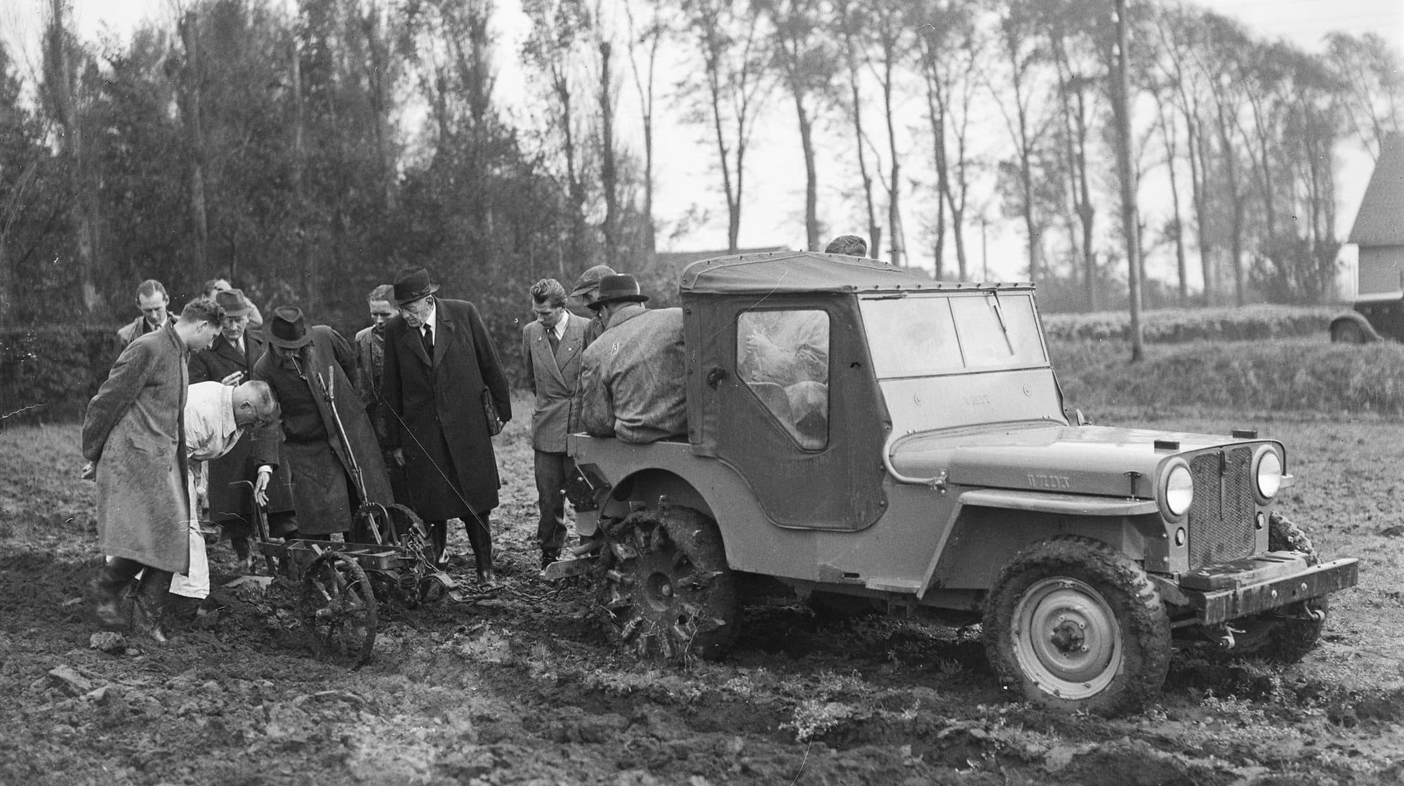 1946 年荷蘭一部 Willys Jeep 在泥地中連接農業機具，旁有多人觀察