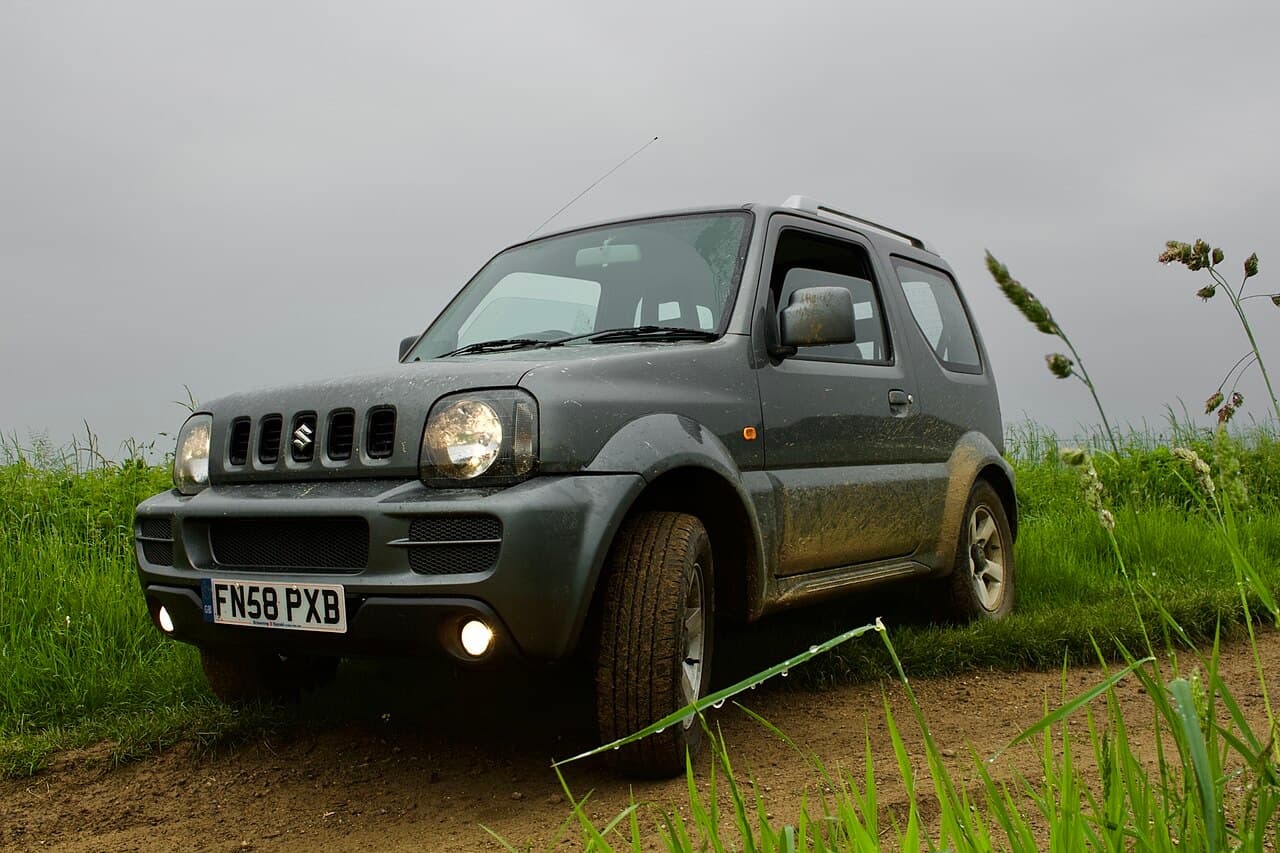 一部灰色第三代 Suzuki Jimny 停在英格蘭 Wiltshire 的濕潤土路與草地之間
